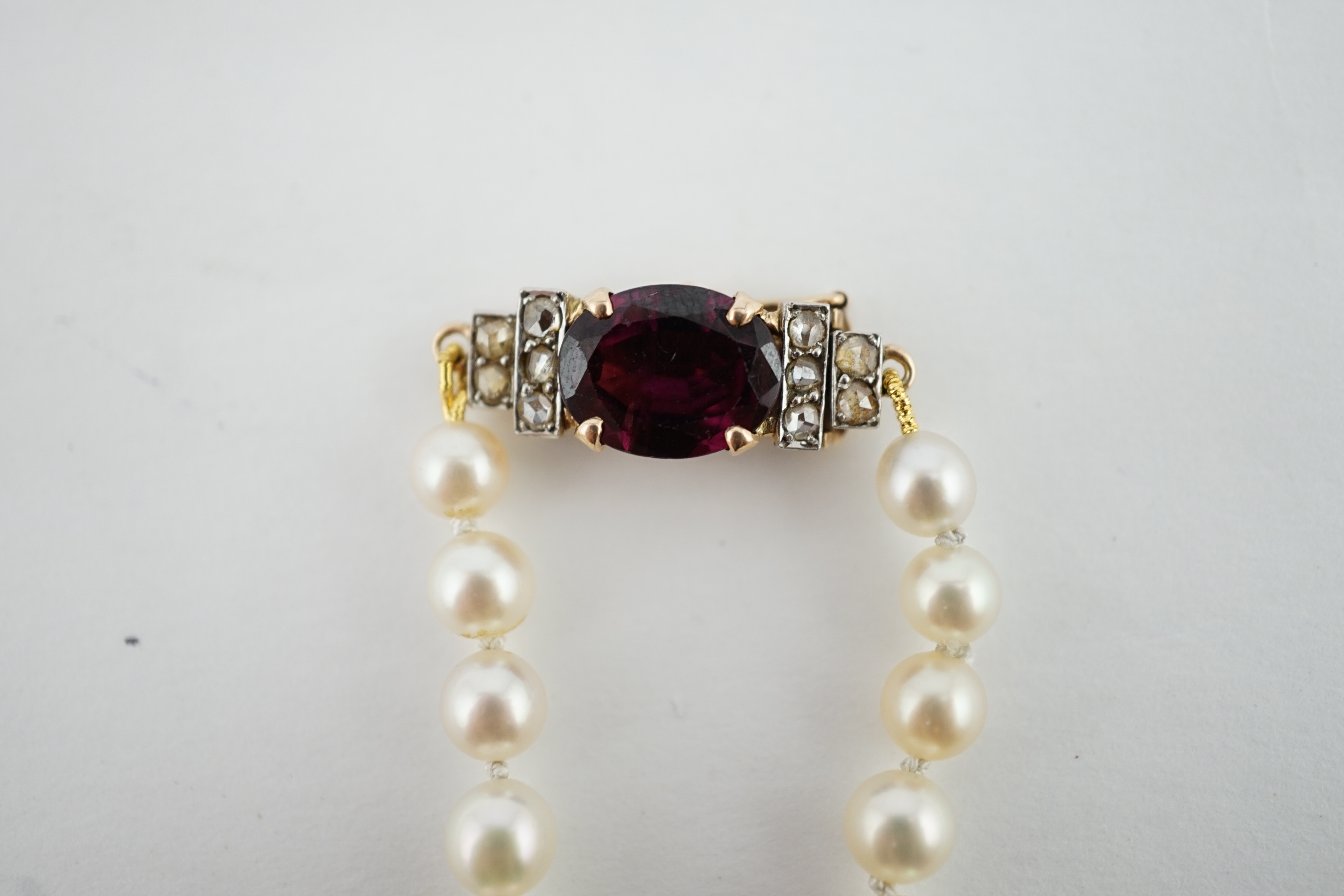 A single strand graduated cultured pearl necklace, with a gold, garnet and rose cut diamond cluster set clasp